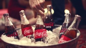 A man grabs a Coca Cola bottle from a bucket full of ice.