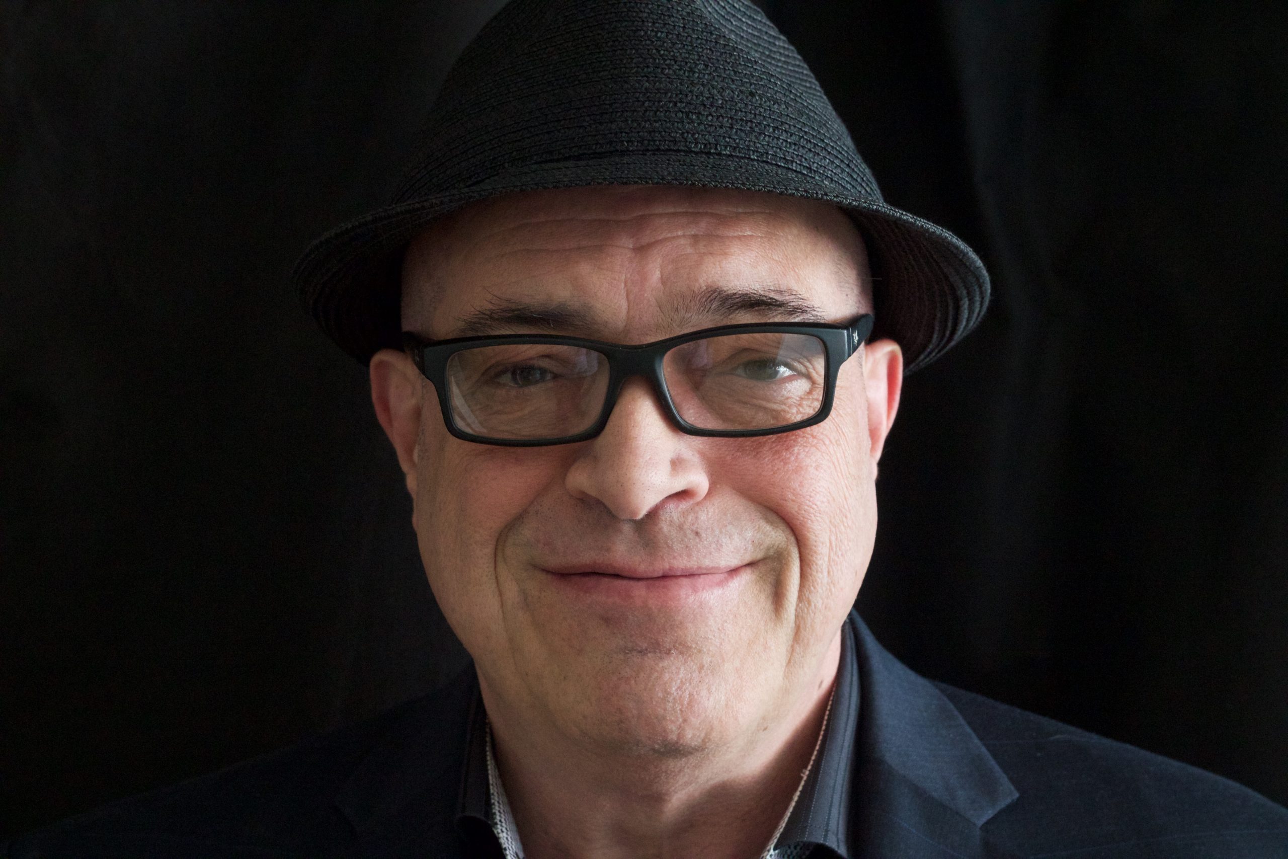 A headshot of Jack Dennis smiling as he wears glasses and a hat.