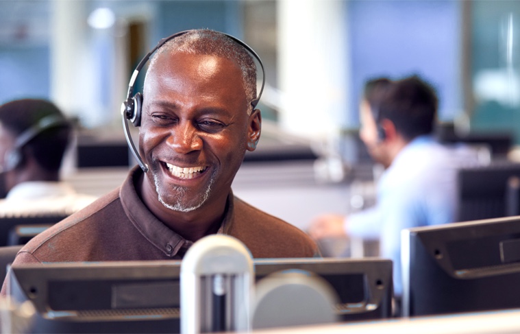 A man smiling as he speaks to a customer through his headset.