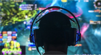 Video game plater wearing headphones, with an out-of-focus video game screen in the background.